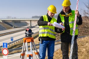 Land surveyors on highway reading geodesist plans use tacheometer