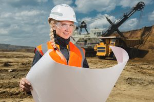 smiling female land surveyor holding plans and wearing a hard hat