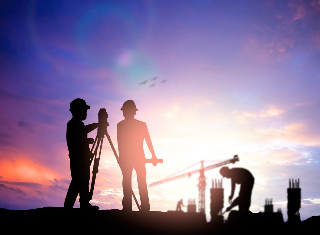 silhouette of two land surveyors with equipment against a purple sunset