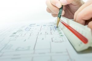 engineer using a paper, ruler, and pencil to draw blue prints