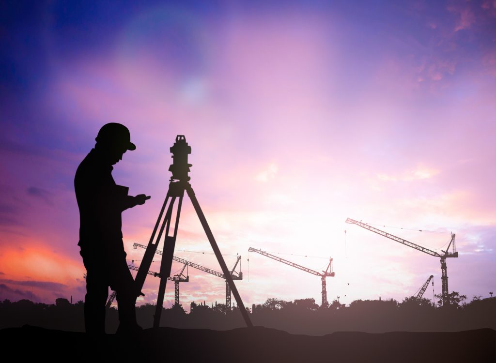 silhouette of land surveying engineer working  in a building site with a purple and white sunset background