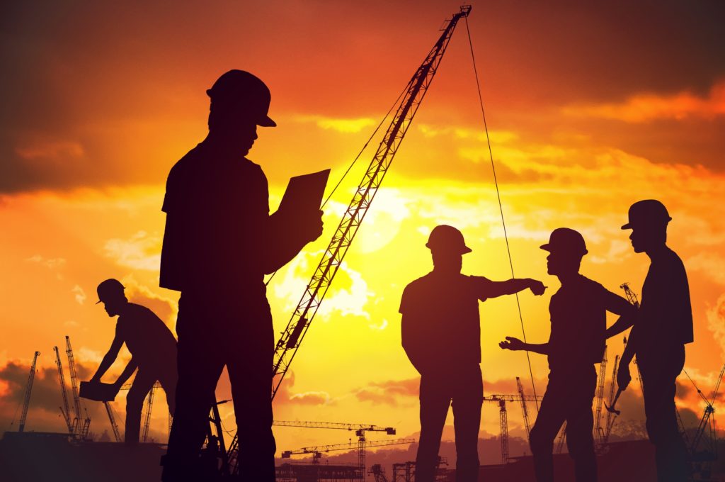 Silhouettes of workers working on construction survey at sunset