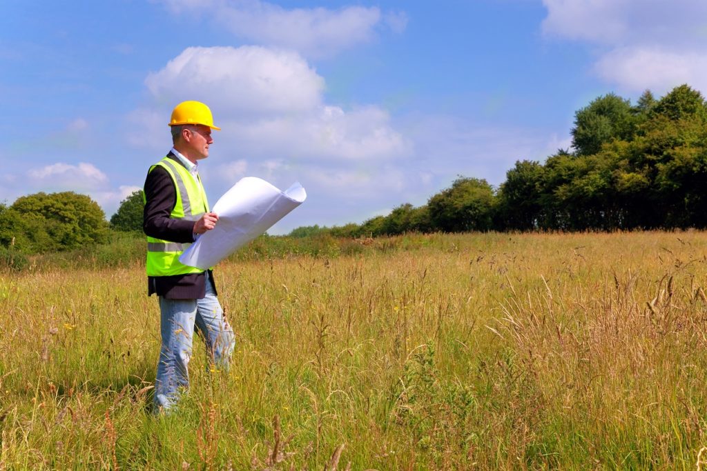 construction manager walking a grassy sight with a map, land planning for a project