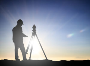 a man who is part of a group of land surveyors in silhouette next to a theodolite 